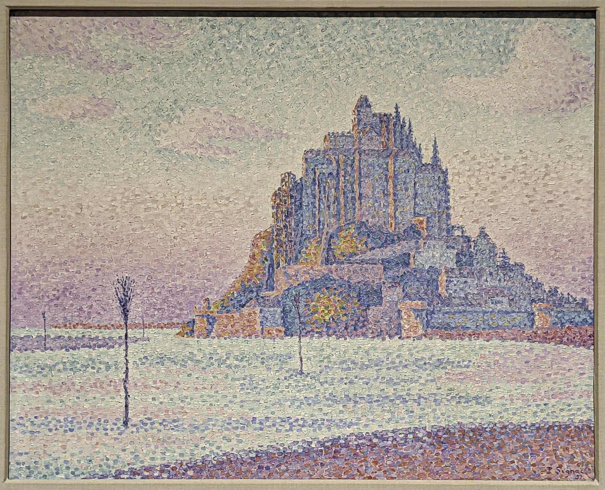 A framed pointillist painting of a Gothic cathedral on a hill, rendered in tiny dots of blue, purple, and orange against a pale sky.