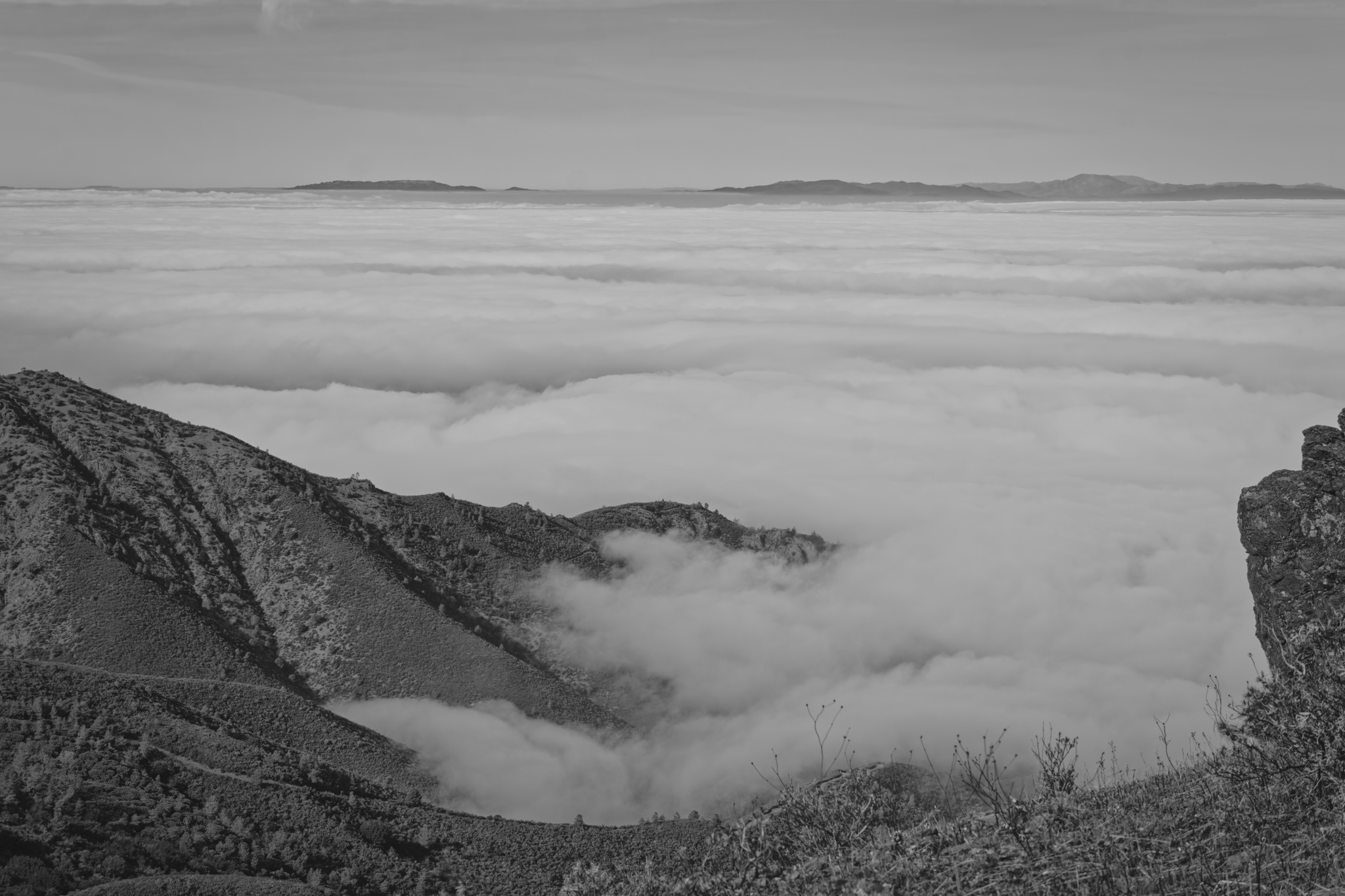 A black and white view from a rocky ridge at Mt Diablo looking out over a thick sea of clouds filling the valley below.