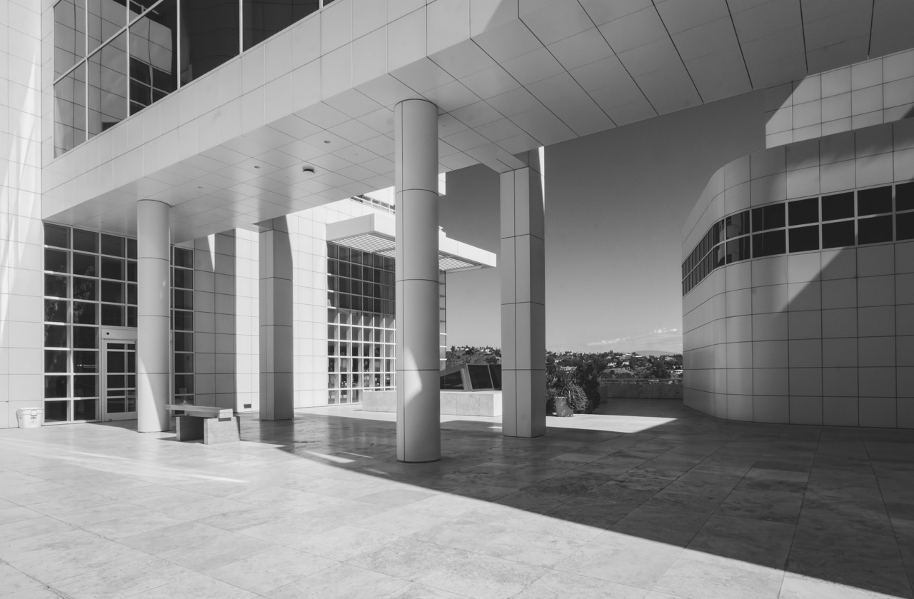 Black and white view of the Getty Center's colonnade, with cylindrical columns casting long shadows across a tiled plaza.