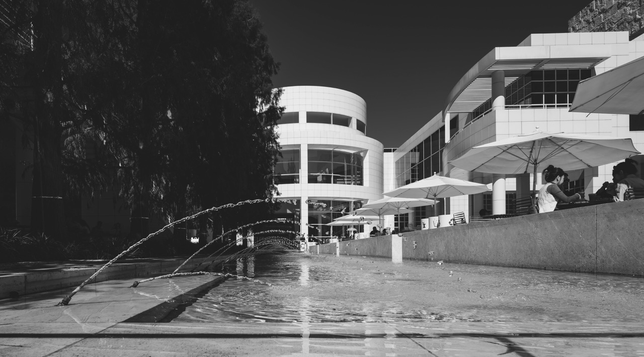 A low-angle view of a shallow fountain with arcing jets of water in front of the white, modern architecture of the Getty Center.