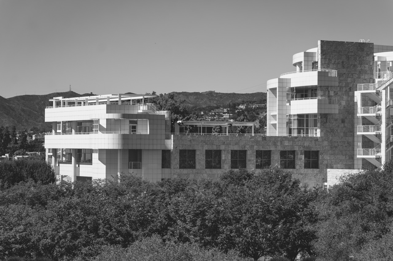 The Getty Center's white and stone modern architecture rises above a dense canopy of trees, with hills visible in the background.