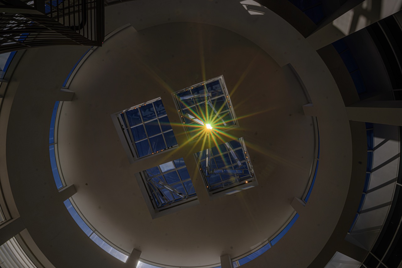 Looking up through a circular atrium at the Getty Center, sunlight bursts through a central skylight, casting a bright starburst across the ceiling.