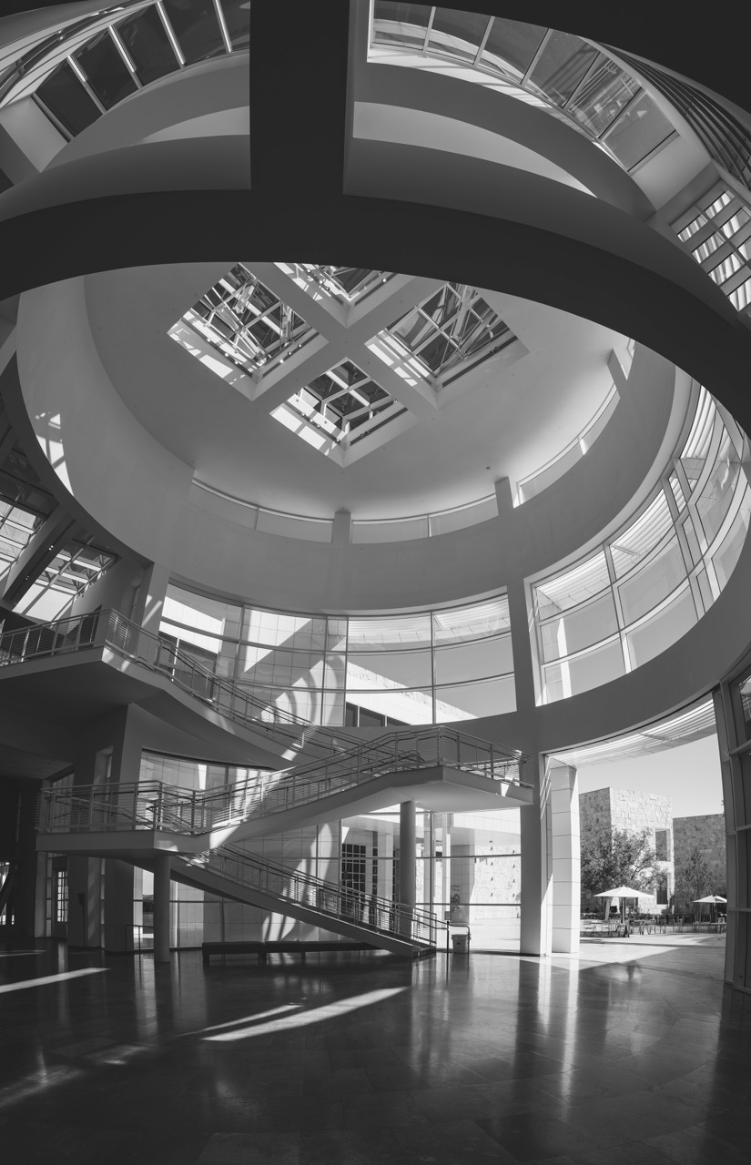 Black and white view of the Getty Center's circular atrium, with a spiral staircase and skylights casting light on the polished floor.