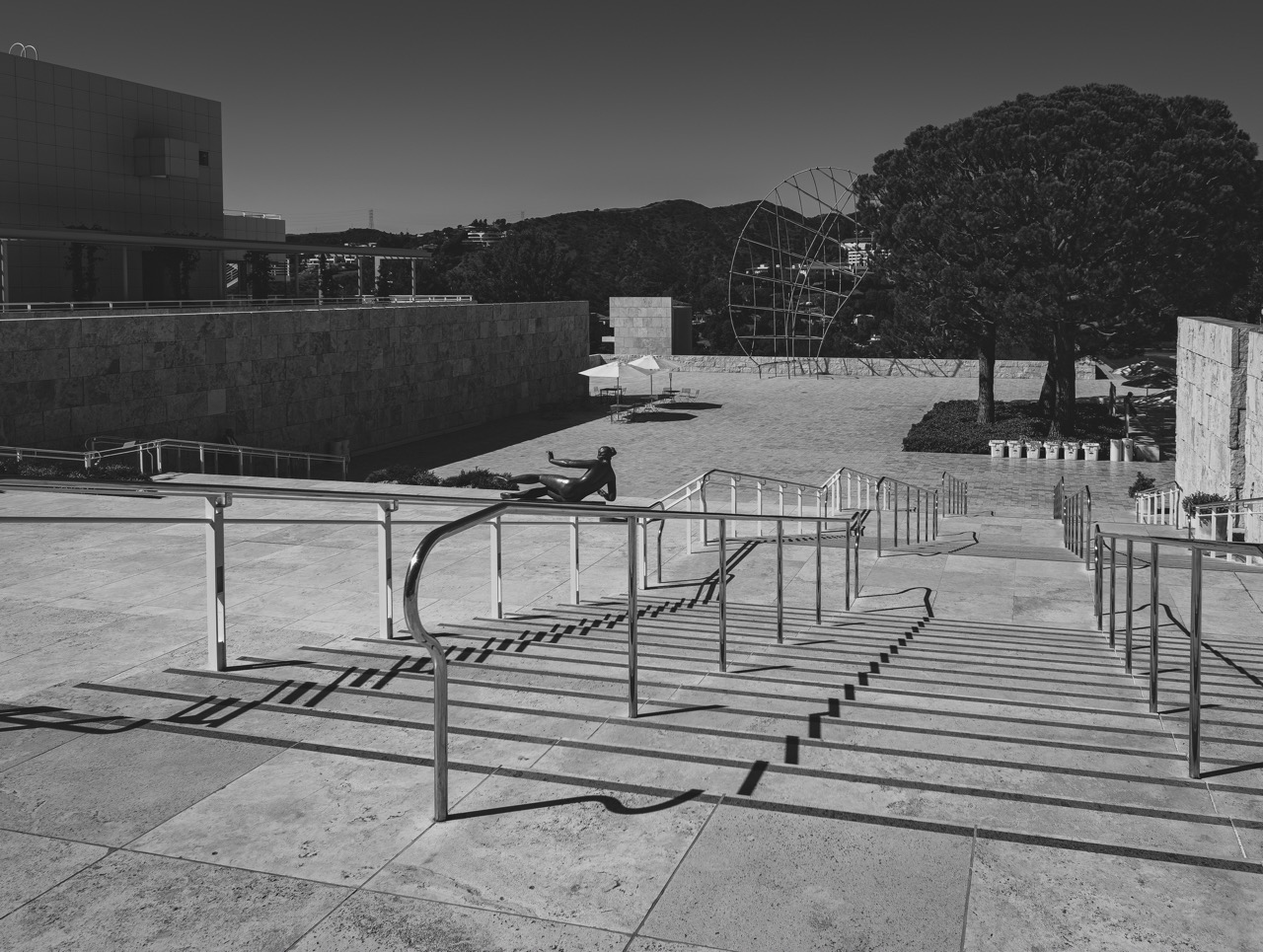 A black and white view of the Getty Center plaza, where a seated sculpture rests on a railing beside a wide staircase.
