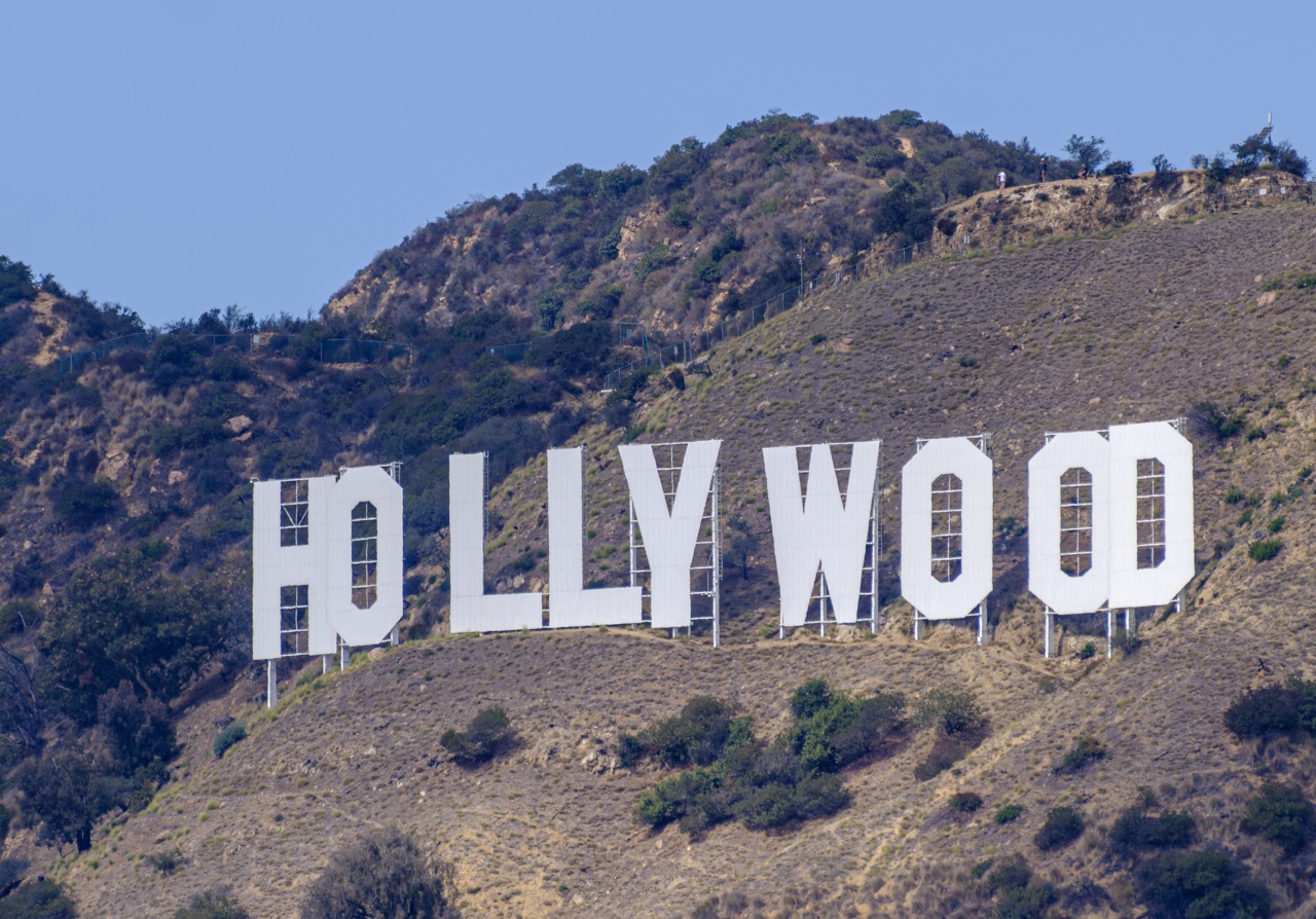 The white Hollywood sign is mounted on a dry, scrubby hillside under a clear blue sky.